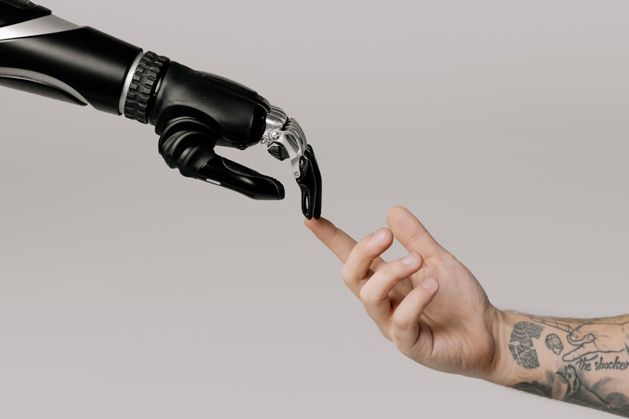 why-choose-us A human hand with tattoos reaching out to a robotic hand on a white background.